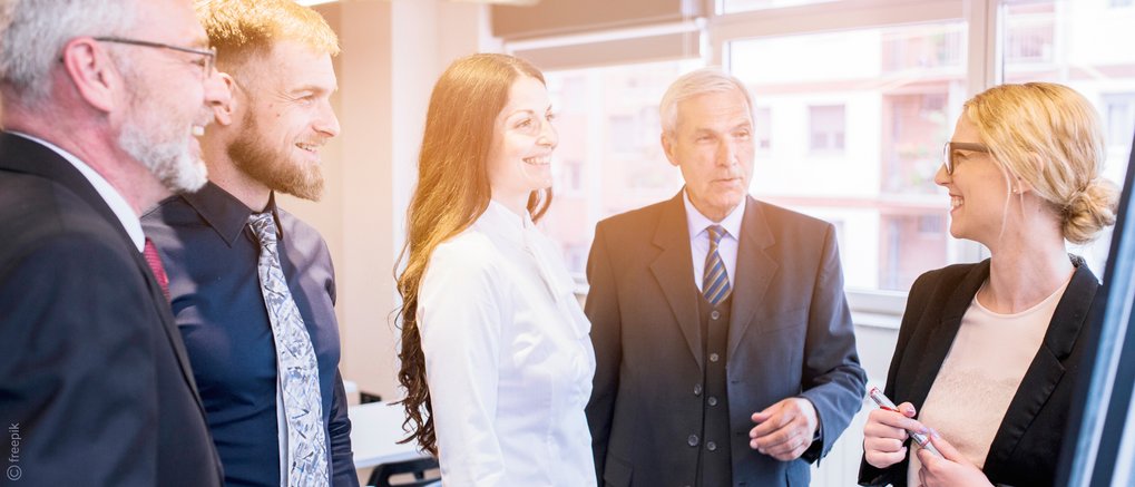 Eine Gruppe von Personen führt eine angeregte Diskussion in einem hellen, modernen Büro mit großen Fenstern.