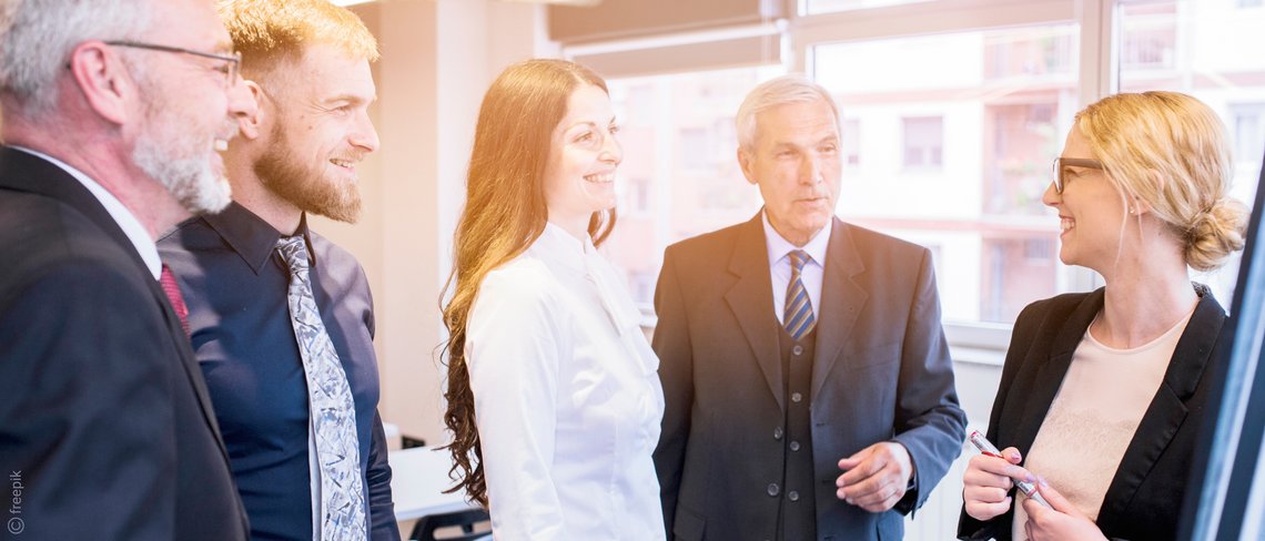 Eine Gruppe von Personen führt eine angeregte Diskussion in einem hellen, modernen Büro mit großen Fenstern.
