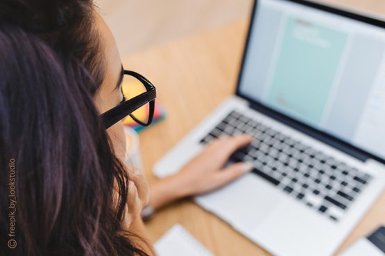 Frau mit Brille arbeitet an einem Laptop, konzentriert auf den Bildschirm.