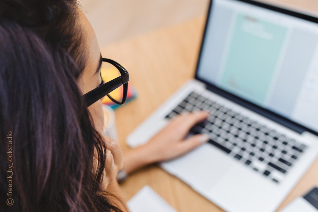 A woman wearing glasses is working on a laptop, focused on the screen.